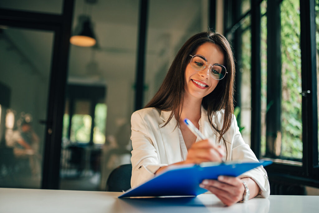 Smiling young woman filling application form or writing personal information in contract.